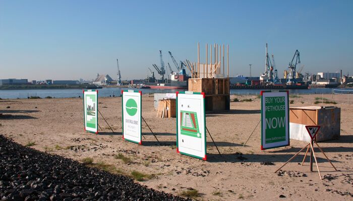 Das Bild zeigt die Elbe mit einem Sandstrand im Vordergrund, auf dem mehrere Plakate aufgestellt sind, die Informationen oder Werbung präsentieren.