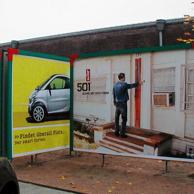 Das Bild zeigt zwei große Plakate: eines mit einem Smart-Auto und das andere mit einer Werbung für Levis Jeans.