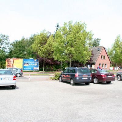 Das Bild zeigt einen Parkplatz, im Hintergrund ist ein großes Wahlplakat zu sehen.