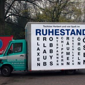 Ein kleiner Lieferwagen mit einem großen Plakat, auf dem das Wort 'Ruhestand' sowie verschiedene Synonyme abgebildet sind.