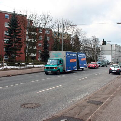 Ein Lieferwagen mit Plakaten fährt auf einer Hauptstraße.
